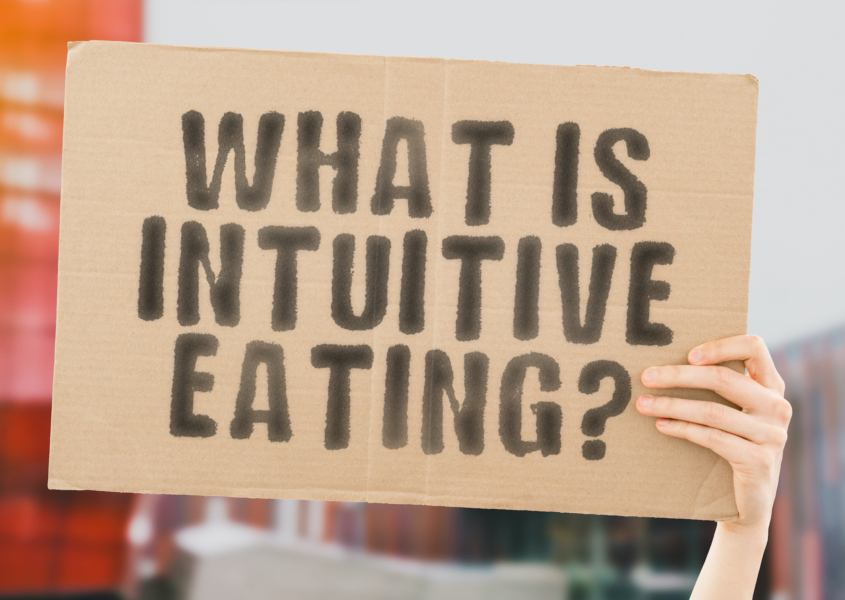 The question " What is intuitive eating? " on a banner in hand with blurred background.