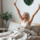 Smiling older woman wakes up happy and refreshed in bed, stretching her arms above her in the morning light after a restful night