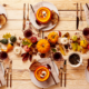 Table with a centerpiece of fall favorites including colorful leaves, pumpkins, squash, and apples, and place settings with linen napkins, gold silverware, and pumpkin soup in small carved pumpkins