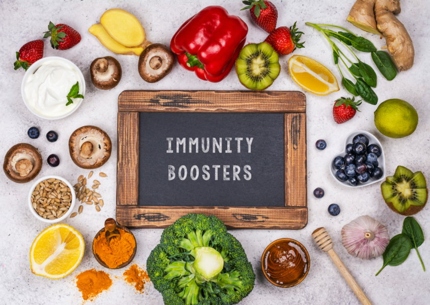 Sign reading "immunity boosters" surrounded by immune-boosting foods including peppers, kiwis, citris fruits, broccoli, garlic, blueberries, and mushrooms.