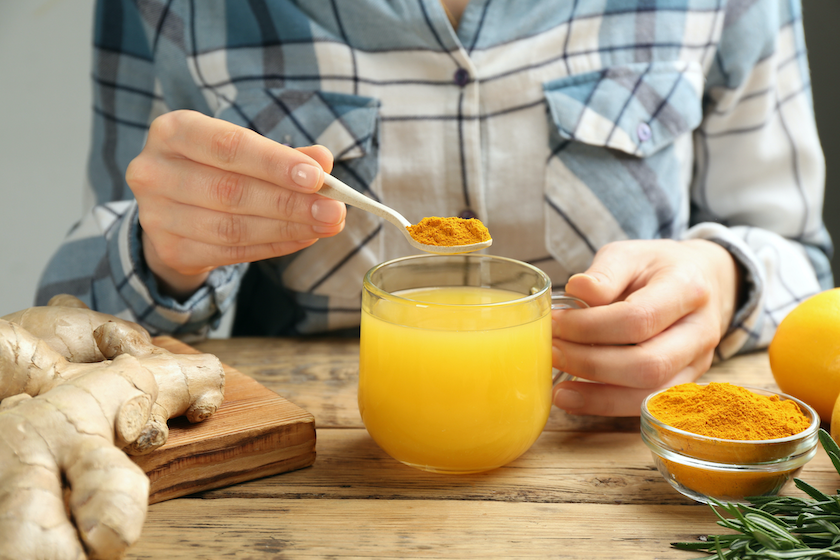 Person stirring turmeric powder into healthy drink. Turmeric root sits next to the drink on the table.