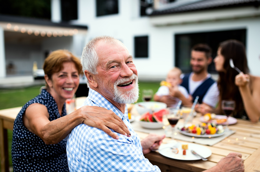 Older couple smiles while eating a healthy meal outdoors with family