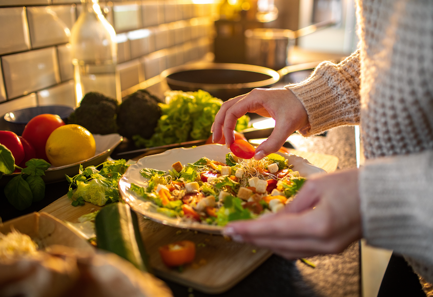 Hands prepare a fresh healthy salad on kitchen counter surrounded by vegetables