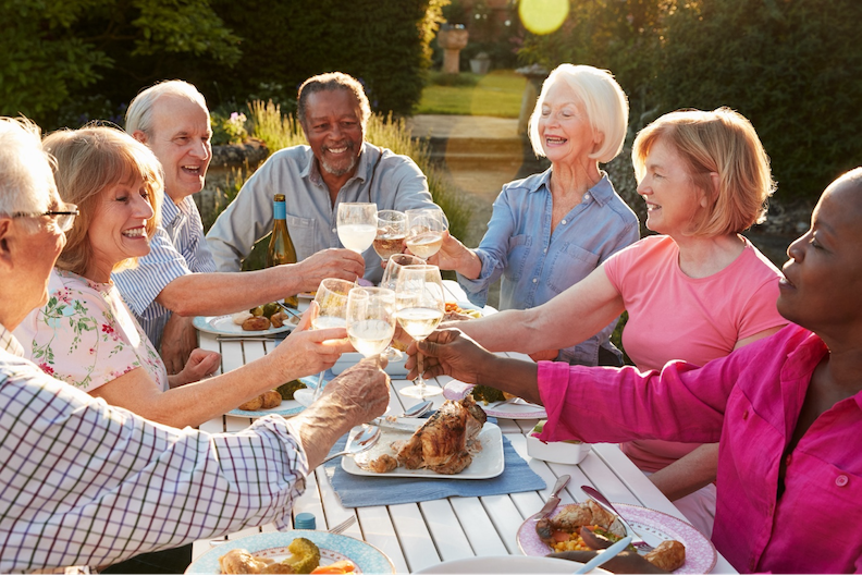 Seniors smile and laugh while drinking and eating at an outdoor dinner party