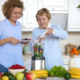 Older adult woman and adult granddaughter make a smoothie with fresh fruits and greens.