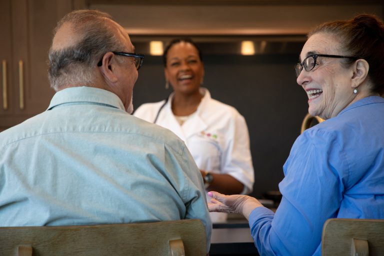 Older couple chatting at a kitchen counter as a smiling personal chef looks on